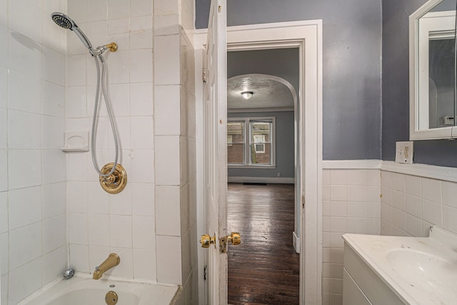 bathroom with wood-type flooring, vanity, tiled shower / bath, and tile walls