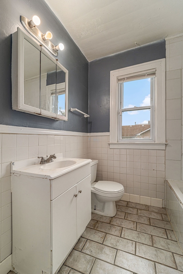 bathroom featuring a washtub, vanity, toilet, and tile walls