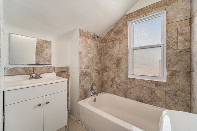 bathroom with tile patterned floors, vanity, tiled shower / bath combo, vaulted ceiling, and tile walls