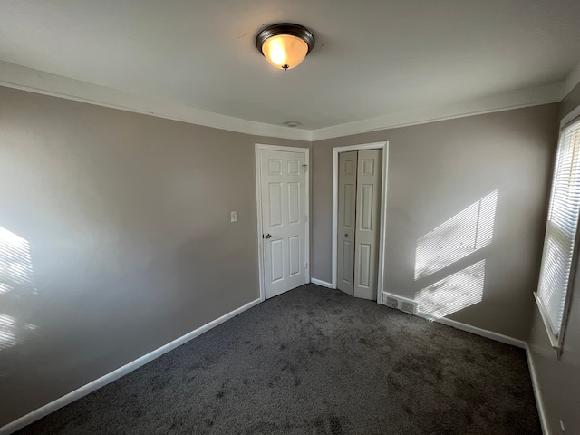 unfurnished bedroom with a closet, dark carpet, and ornamental molding