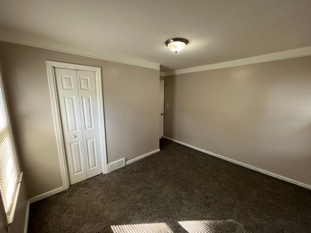 unfurnished bedroom featuring dark carpet, crown molding, and a closet