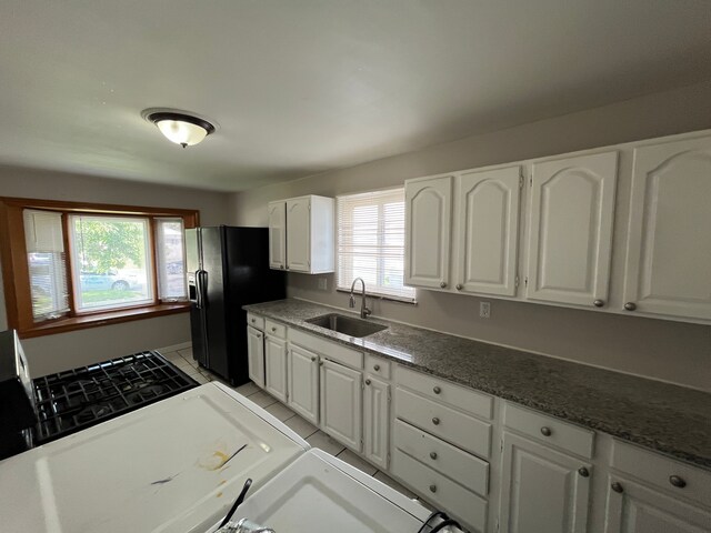 kitchen with white cabinets, black fridge with ice dispenser, light tile patterned floors, and sink