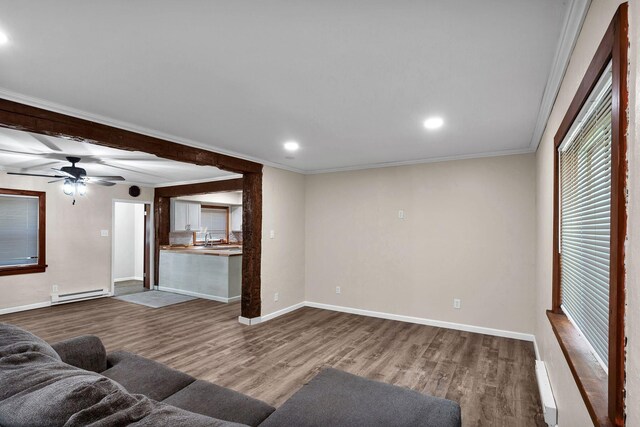 unfurnished living room featuring a baseboard heating unit, sink, crown molding, ceiling fan, and wood-type flooring