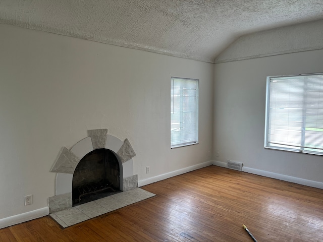 unfurnished living room with lofted ceiling, a textured ceiling, a tile fireplace, and light hardwood / wood-style flooring