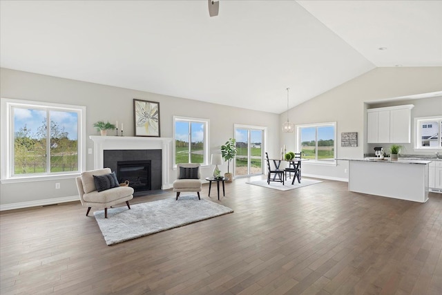 living room featuring dark hardwood / wood-style flooring, a tiled fireplace, high vaulted ceiling, and a notable chandelier