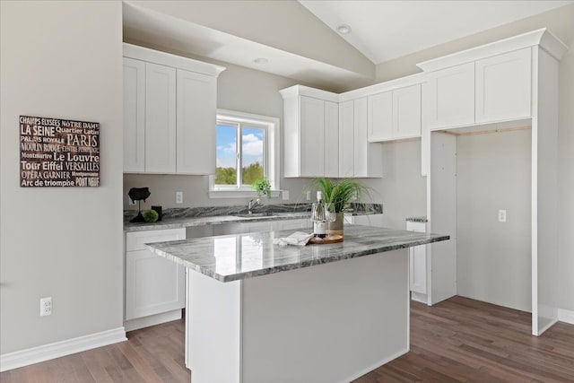 kitchen featuring lofted ceiling, white cabinetry, a center island, hardwood / wood-style flooring, and light stone countertops