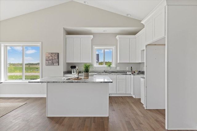 kitchen featuring light stone countertops, a center island, white cabinets, and light hardwood / wood-style floors