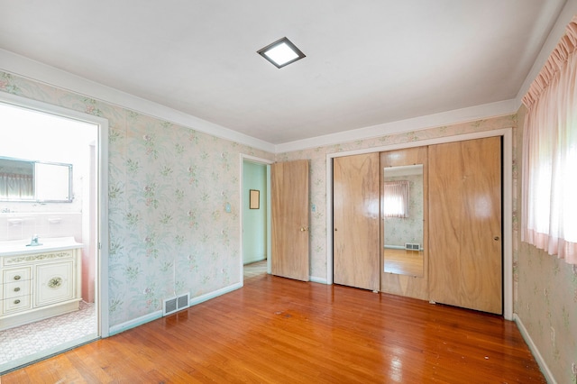 unfurnished bedroom with wood-type flooring, a closet, multiple windows, and sink