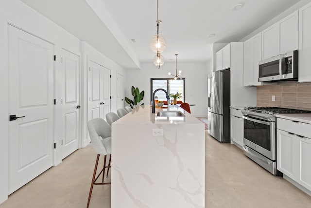 kitchen with appliances with stainless steel finishes, tasteful backsplash, sink, a center island with sink, and decorative light fixtures