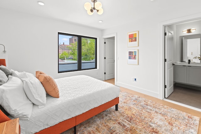 bedroom with light wood-type flooring, an inviting chandelier, and ensuite bath