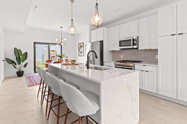 kitchen with white cabinetry, light stone countertops, a center island with sink, and appliances with stainless steel finishes