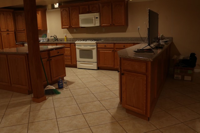 kitchen with sink, white appliances, dark stone countertops, and light tile patterned flooring