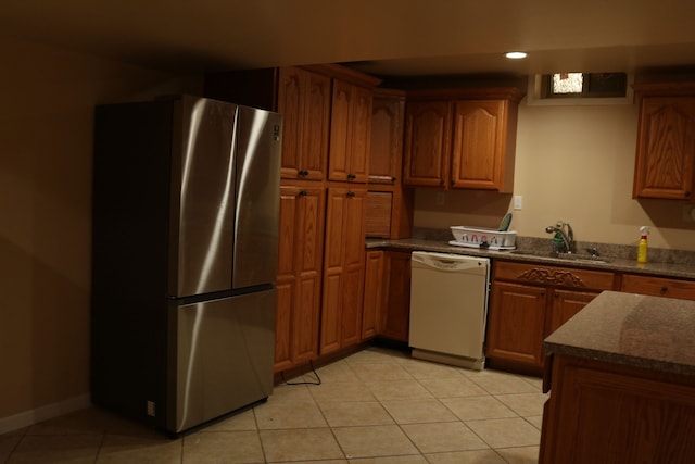 kitchen with dark stone counters, white dishwasher, sink, light tile patterned floors, and stainless steel refrigerator