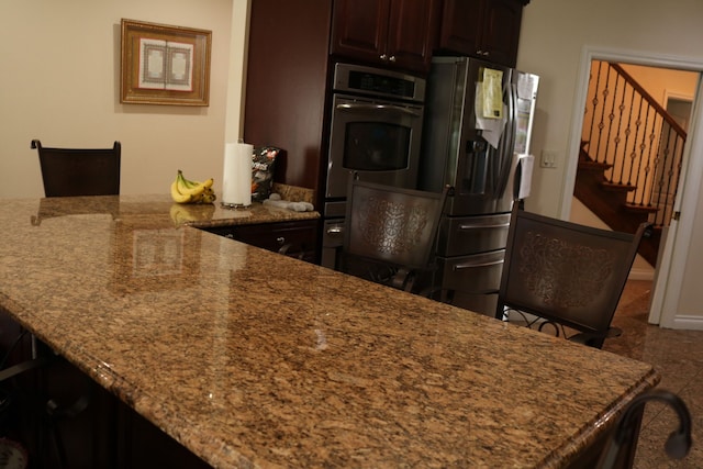 kitchen featuring a breakfast bar area, light stone counters, dark brown cabinets, and stainless steel refrigerator with ice dispenser