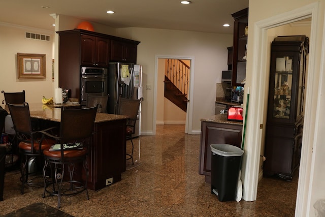 kitchen with stone counters, appliances with stainless steel finishes, dark brown cabinets, and a kitchen breakfast bar