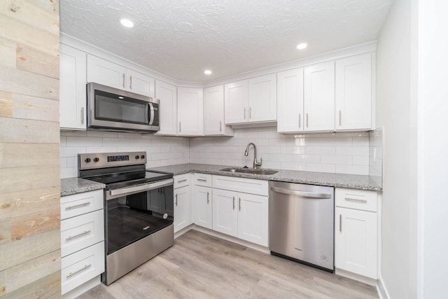 kitchen with white cabinets, sink, light hardwood / wood-style flooring, light stone countertops, and stainless steel appliances