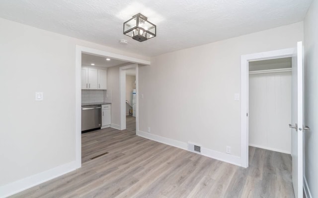 unfurnished dining area with visible vents, baseboards, a textured ceiling, and light wood finished floors