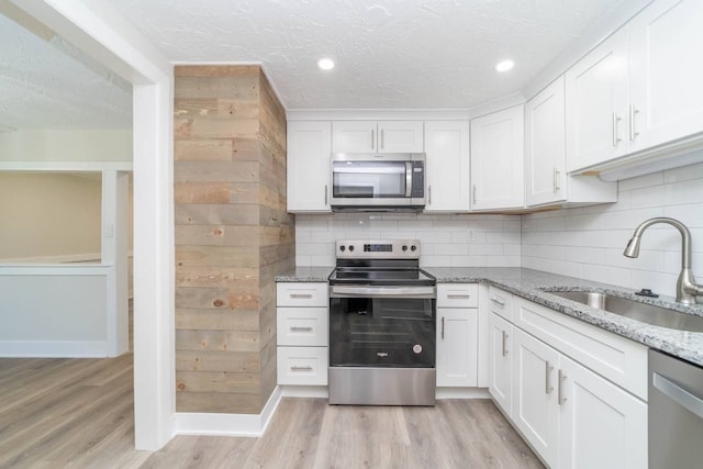 kitchen with light wood finished floors, tasteful backsplash, white cabinets, stainless steel appliances, and a sink