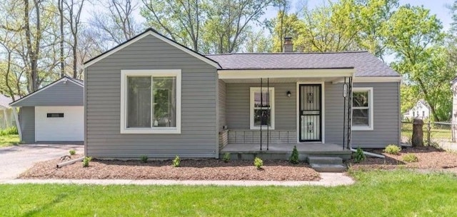 view of front of house with aphalt driveway, a porch, a chimney, and a detached garage