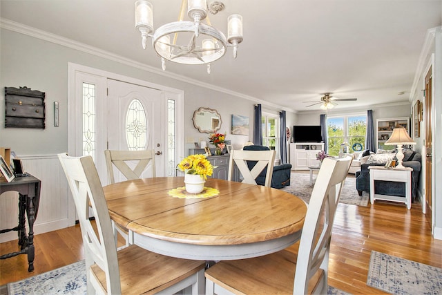 dining room with ceiling fan with notable chandelier, wood walls, ornamental molding, and light hardwood / wood-style flooring