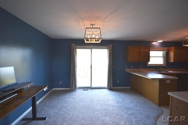 kitchen featuring kitchen peninsula, light carpet, hanging light fixtures, and a textured ceiling