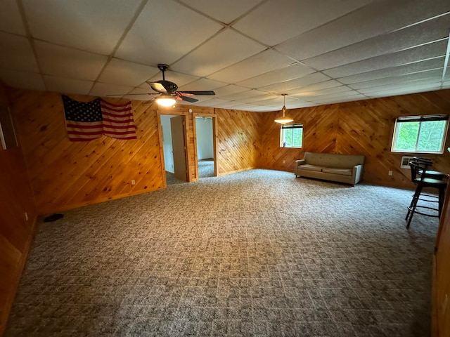 unfurnished living room featuring a paneled ceiling, carpet flooring, wood walls, and ceiling fan