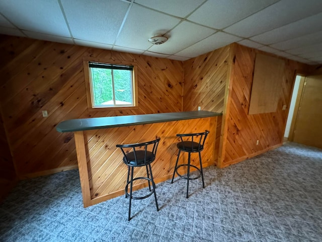 bar with a drop ceiling, carpet floors, and wooden walls