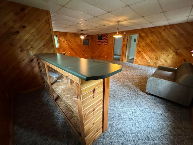 bar with dark colored carpet, pendant lighting, a drop ceiling, and wood walls