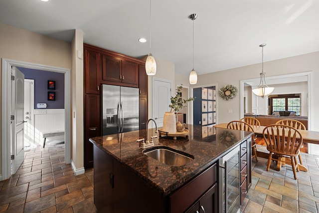 kitchen with beverage cooler, a kitchen island with sink, sink, hanging light fixtures, and built in fridge