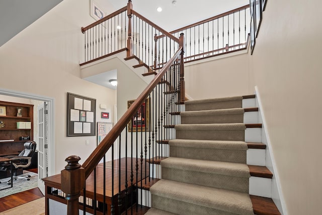 stairway with hardwood / wood-style floors and a towering ceiling