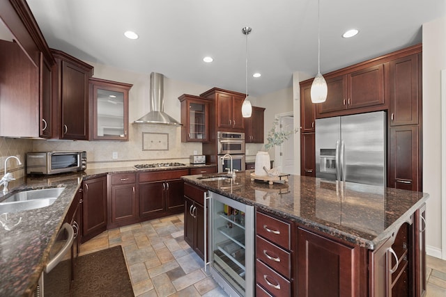 kitchen with wall chimney range hood, hanging light fixtures, sink, stainless steel appliances, and beverage cooler