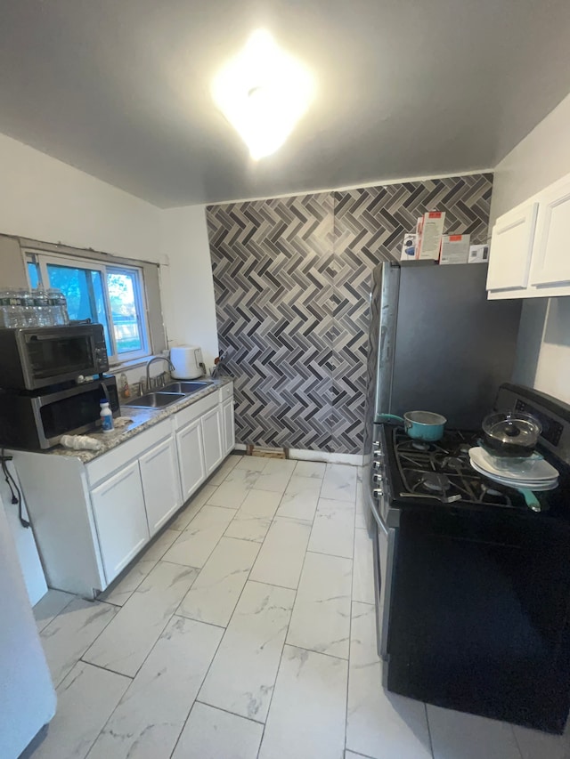 kitchen with an accent wall, a sink, white cabinets, marble finish floor, and appliances with stainless steel finishes