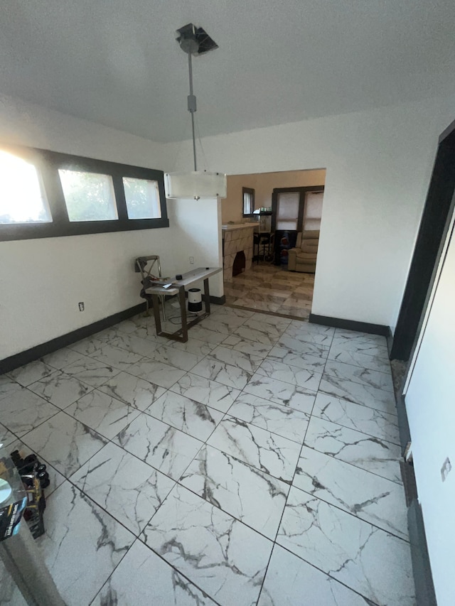 unfurnished dining area with a textured ceiling, marble finish floor, and baseboards