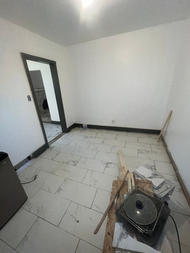 spare room featuring marble finish floor and baseboards