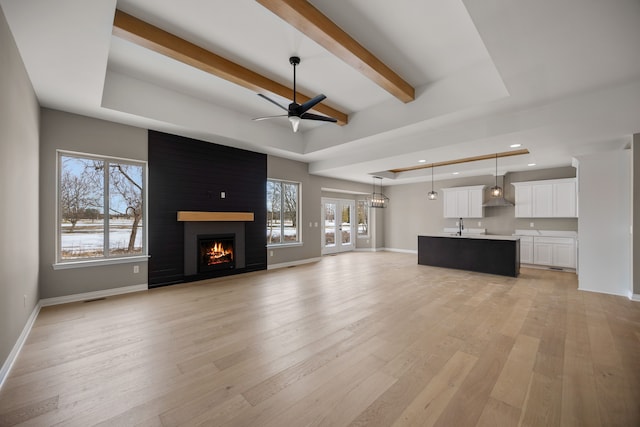 unfurnished living room featuring a raised ceiling, a fireplace, light hardwood / wood-style floors, and beamed ceiling