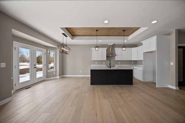 kitchen featuring decorative light fixtures, white cabinetry, a kitchen island with sink, a tray ceiling, and wall chimney exhaust hood