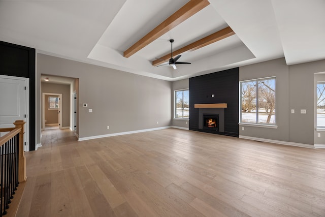 unfurnished living room with a raised ceiling, a large fireplace, beamed ceiling, and light hardwood / wood-style flooring