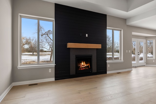 unfurnished living room with french doors, a fireplace, and light wood-type flooring