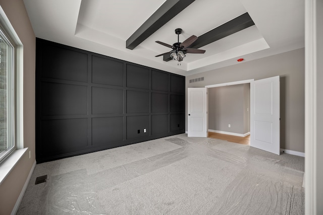 unfurnished bedroom with ceiling fan, a tray ceiling, and light carpet