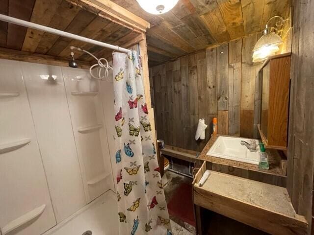 bathroom with a shower with curtain, wooden ceiling, wooden walls, and sink