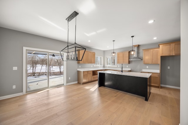 kitchen with pendant lighting, wall chimney range hood, sink, light hardwood / wood-style floors, and a center island with sink