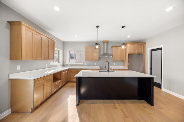 kitchen with sink, a kitchen island with sink, wall chimney range hood, and light brown cabinets