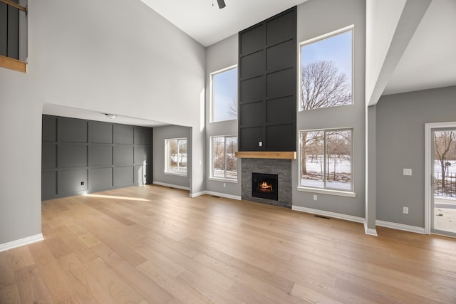 unfurnished living room with ceiling fan, a large fireplace, light hardwood / wood-style floors, and a high ceiling