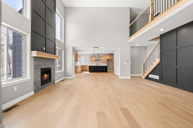 unfurnished living room with a towering ceiling, a fireplace, and light hardwood / wood-style flooring