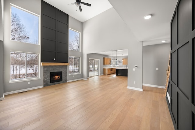 unfurnished living room featuring a towering ceiling, a large fireplace, ceiling fan, and light wood-type flooring