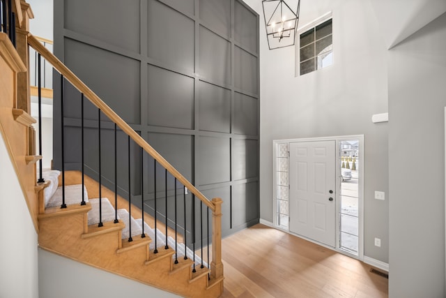 foyer with a towering ceiling, a chandelier, and light wood-type flooring