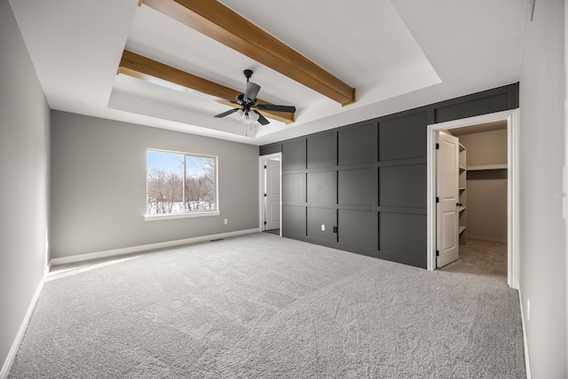 unfurnished bedroom with a spacious closet, a tray ceiling, a closet, beamed ceiling, and light colored carpet