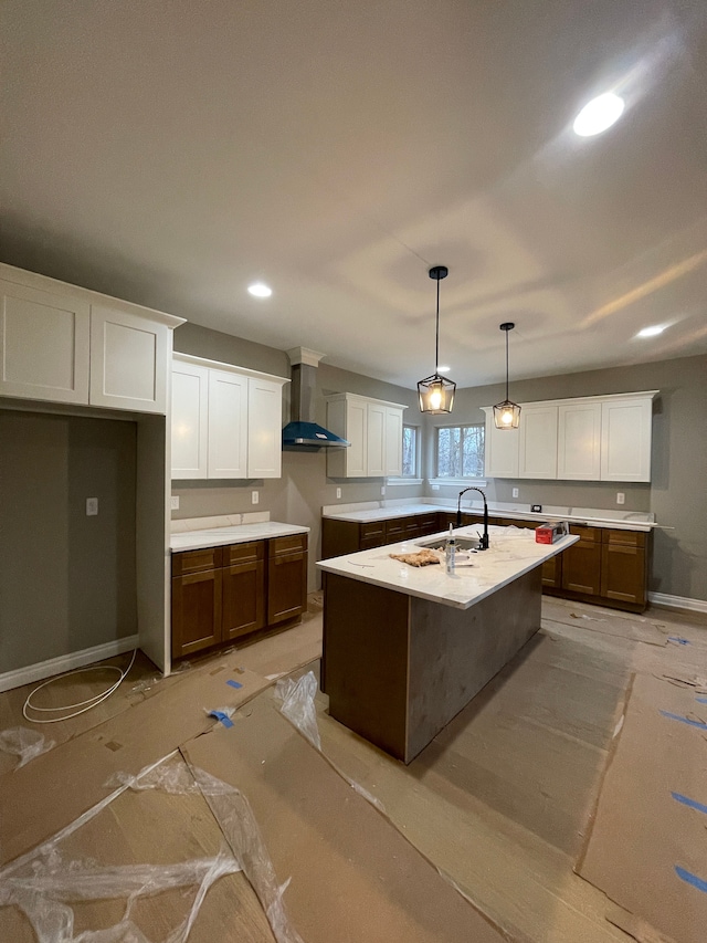 kitchen with sink, wall chimney exhaust hood, pendant lighting, a center island with sink, and white cabinets