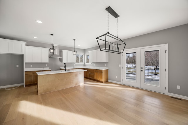 kitchen featuring white cabinetry, hanging light fixtures, wall chimney range hood, and a center island with sink