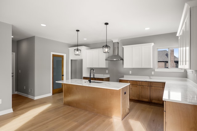 kitchen with wall chimney exhaust hood, decorative light fixtures, a kitchen island with sink, and white cabinets